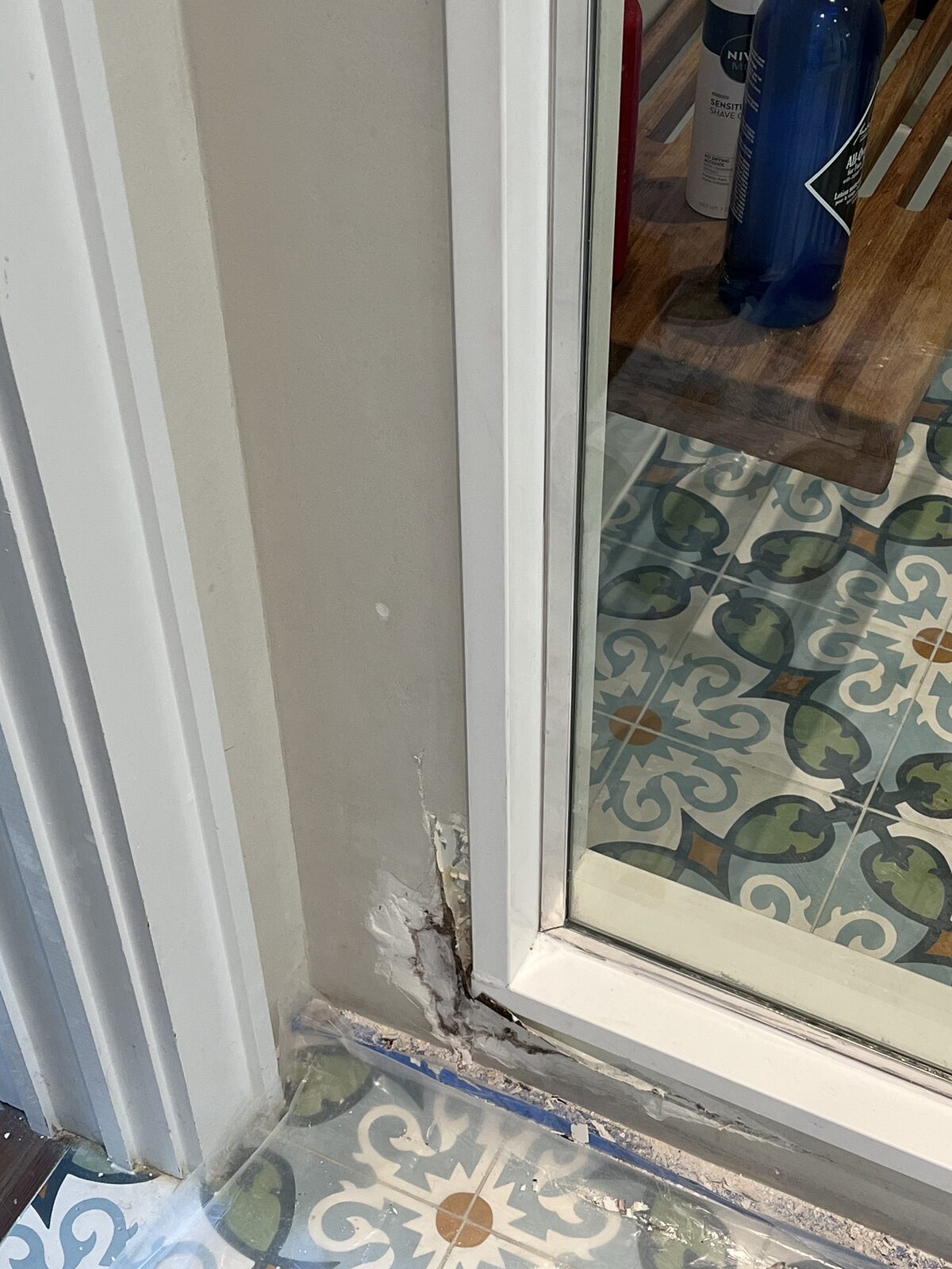 Mold and peeling paint at the bottom of a bathroom doorway trim next to encaustic floor tile