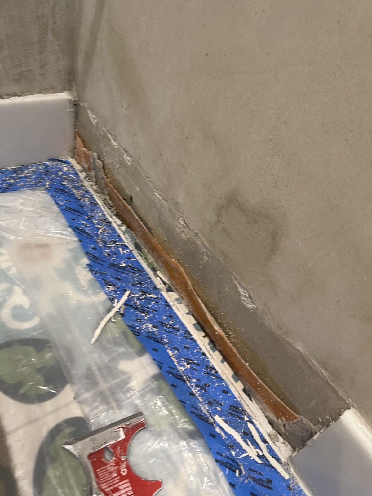 Rust bleeding from behind a bathroom wall base with water staining above — classic humidity-driven failure